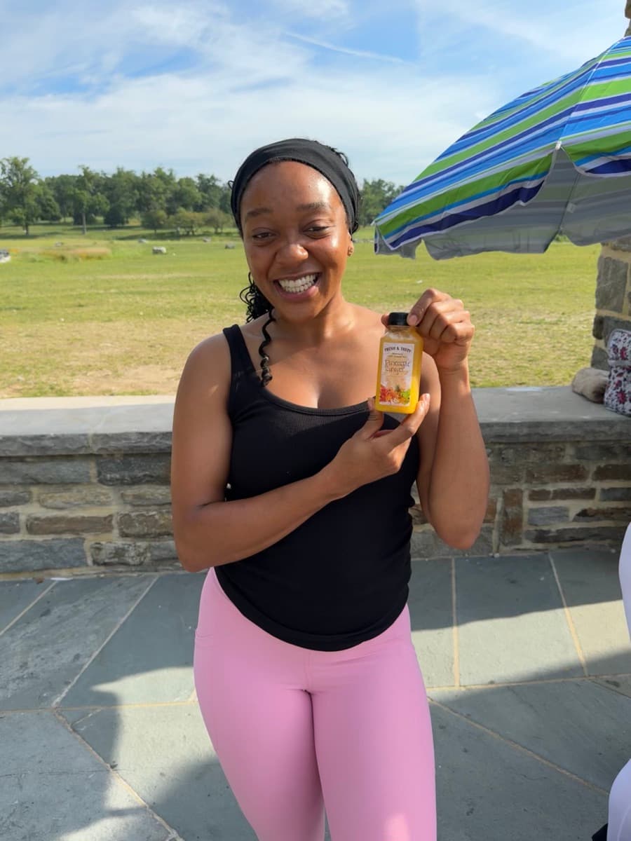 Smiling client holding a pineapple ginger juice at the outdoor FitCamp